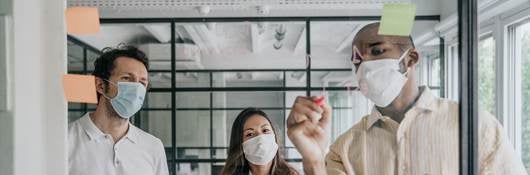 A man, a woman and another man collaborate on the other side of a transparent work board